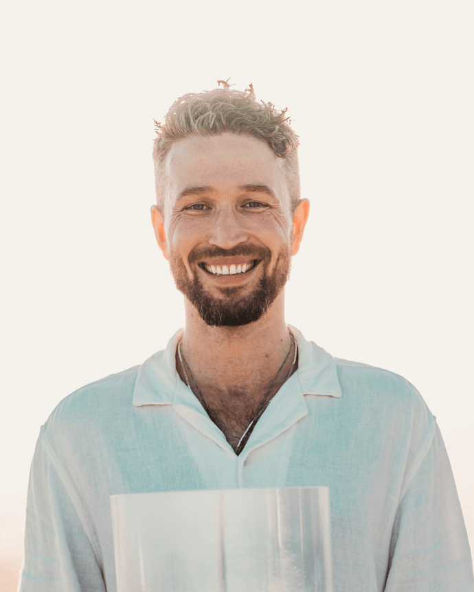 Avery Whitmore, founder of The Sound Healing Studio, surrounded by an array of crystal singing bowls and other healing instruments, embodying the transformative power of sound healing in a serene studio setting.